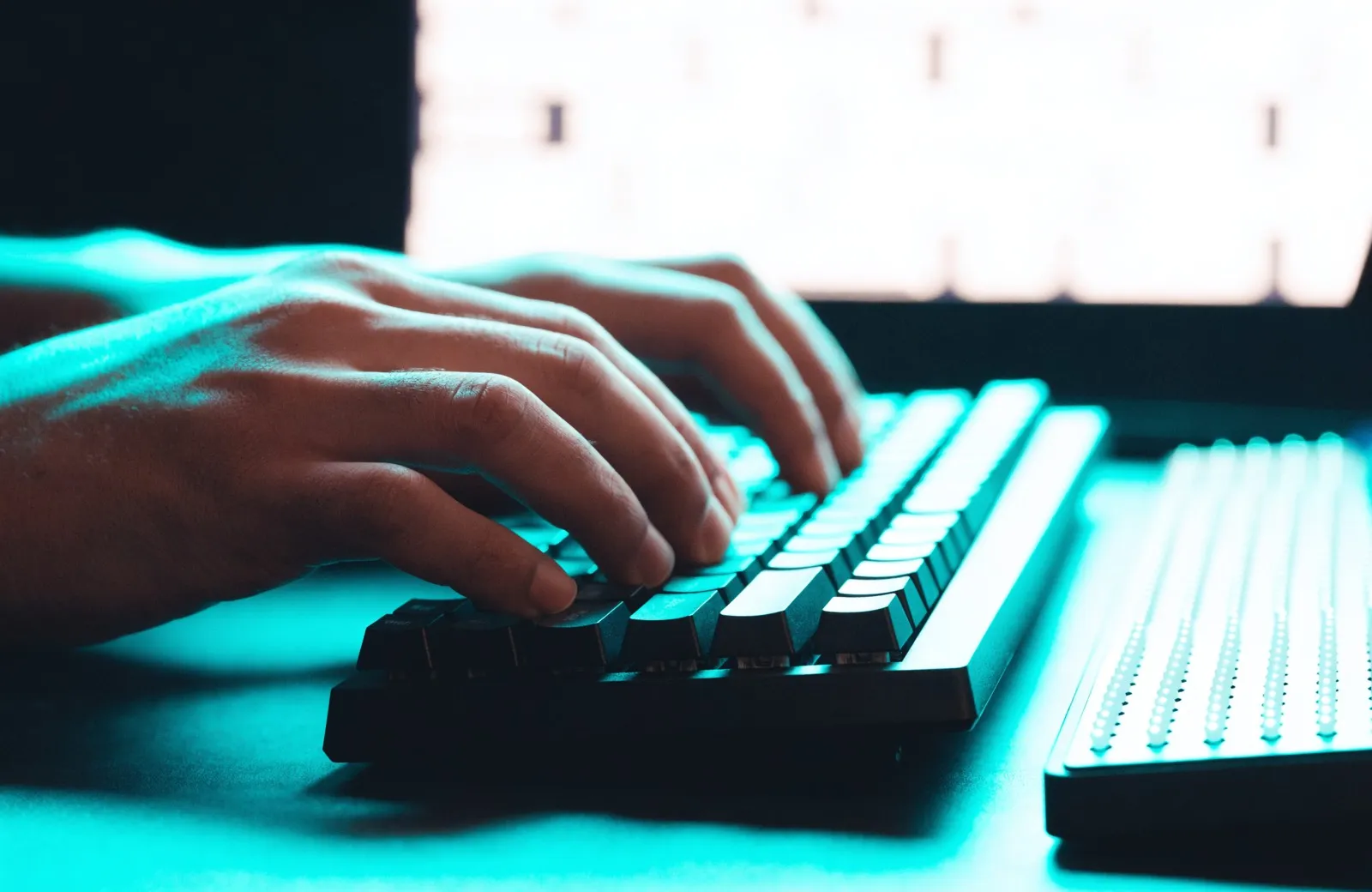 Haende auf einer Tastatur, daneben eine Braillezeile, in tuerkisem Licht.